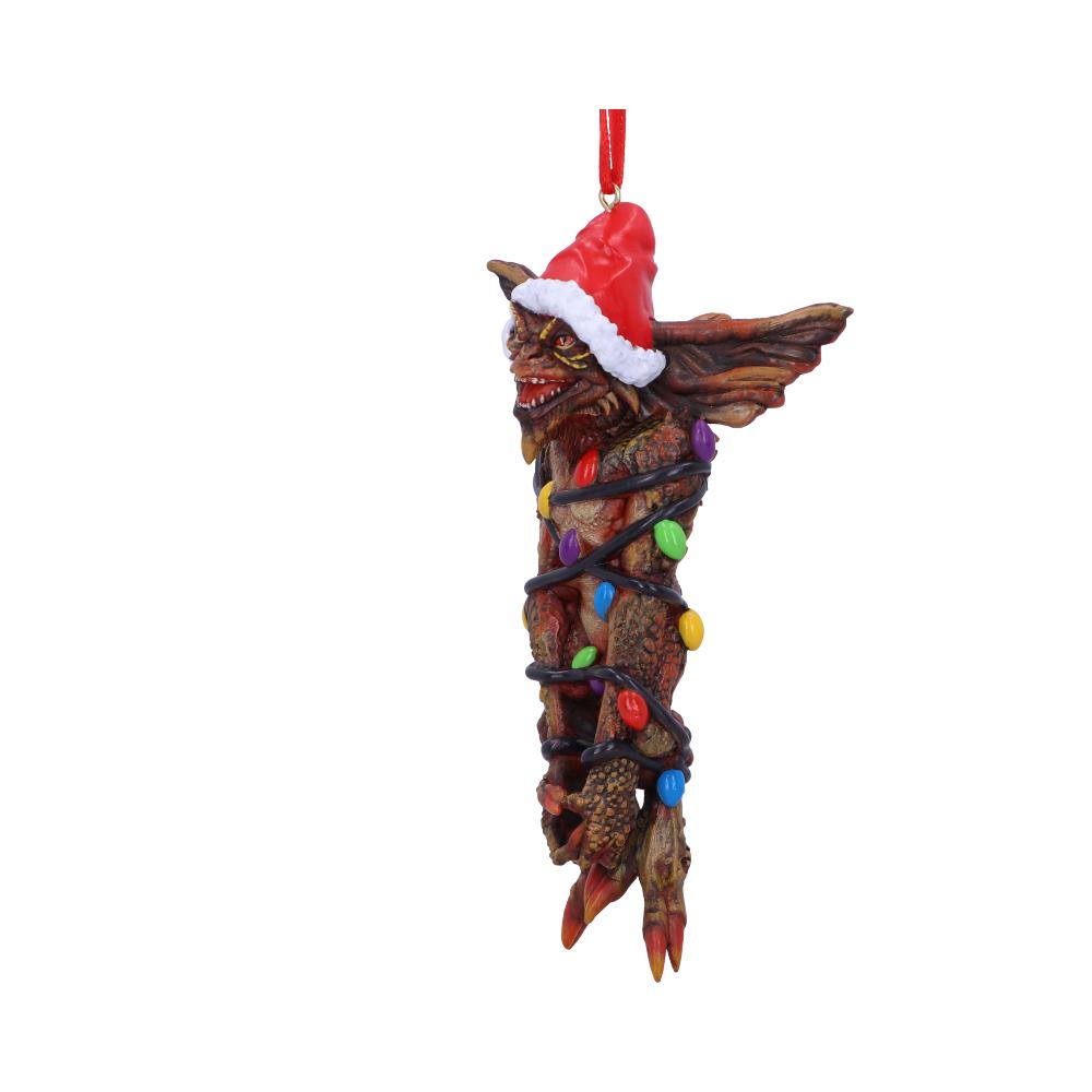 A gremlin-like creature, wearing a Santa hat, is wrapped in colorful Christmas lights. It hangs from a red string, set against a plain white background.