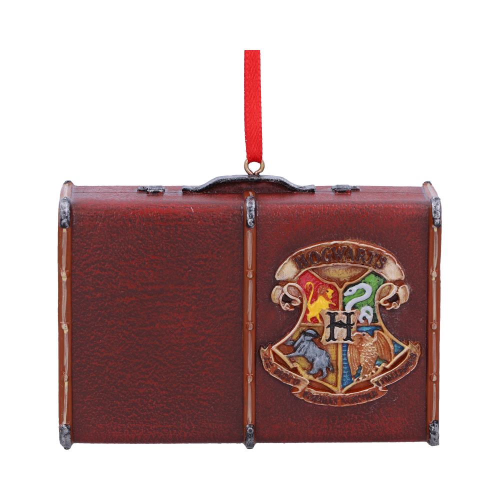 A brown suitcase ornament hangs from a red ribbon, featuring the Hogwarts crest with house symbols: lion, snake, badger, and eagle, accompanied by the text "Hogwarts" above them.