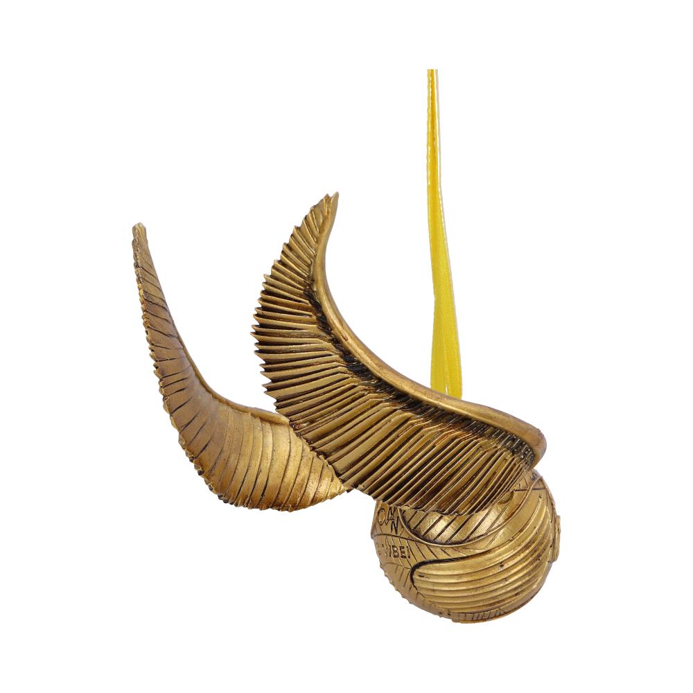 A golden snitch ornament with large decorative wings hangs suspended by a yellow ribbon. Its surface features detailed engravings, providing a textured appearance against a plain white background.