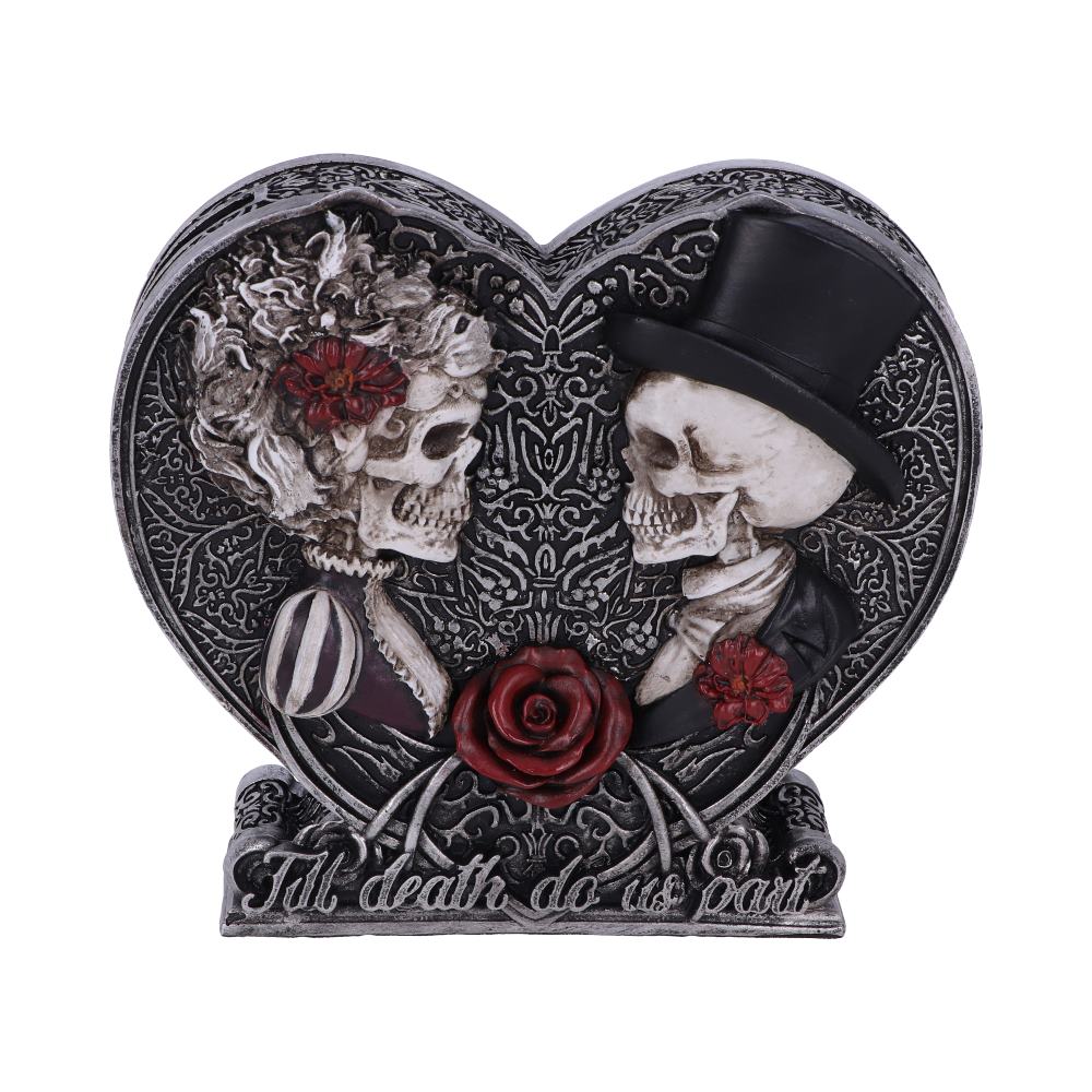 A heart-shaped figurine depicts two skulls, a bride and groom, embracing. It rests on a base inscribed: "Till death do us part."