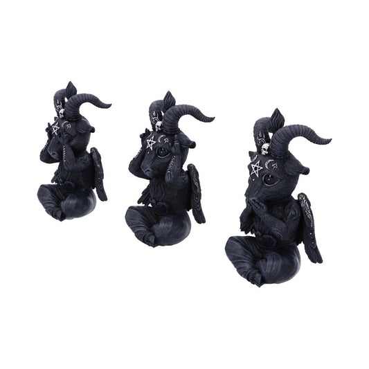 Three black Baphomet figurines sit cross-legged, hands clasped in front of their mouths in prayer. The figurines have small wings and the word “COAGULA” inscribed on their left arms. They are situated on a plain white surface.