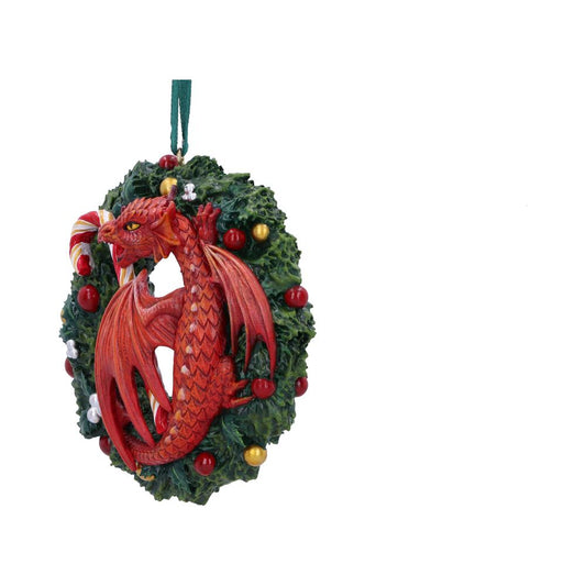 A red dragon clings to a festive wreath adorned with red and gold baubles, white snowflakes, and a candy cane, hanging by a green ribbon against a white background.