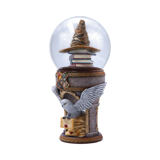 A glass globe encases a sorting hat atop stacked books, resting on a tower embellished with a crest. A white owl carries a sealed letter at the base.