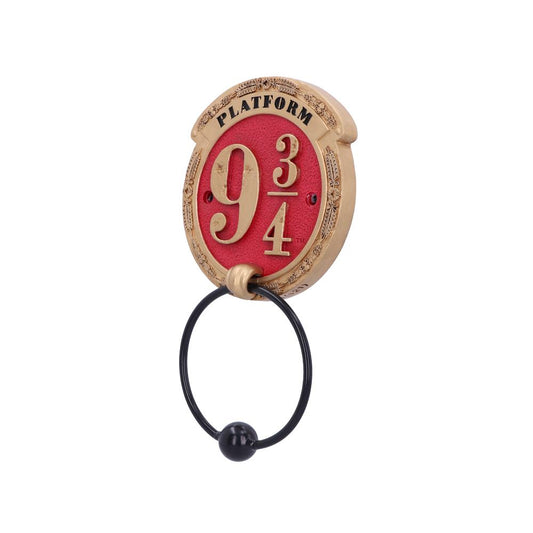 A decorative wall plaque features the text "PLATFORM 9 3/4" in gold on a red background. A black ring with a ball hangs from it, against a white backdrop.