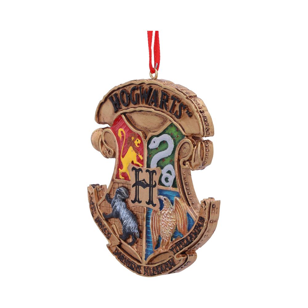 A decorative ornament shaped like the Hogwarts crest features house symbols and colors with a red hanging ribbon. Text: “HOGWARTS” and “DRACO DORMIENS NUNQUAM TITILLANDUS.”