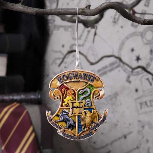 An ornament depicting the Hogwarts crest hangs from a branch. It features a lion, snake, badger, and eagle, and the word "HOGWARTS." A map and striped fabric are visible behind it.