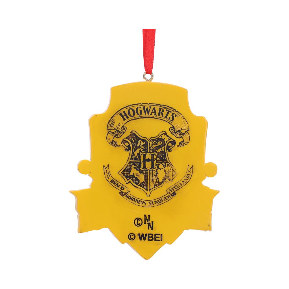 A yellow crest-shaped ornament featuring the Hogwarts emblem with a red hanging ribbon. Text includes "HOGWARTS," "Draco Dormiens Nunquam Titillandus," and copyright symbols ©, NN, © WBEI, © N.