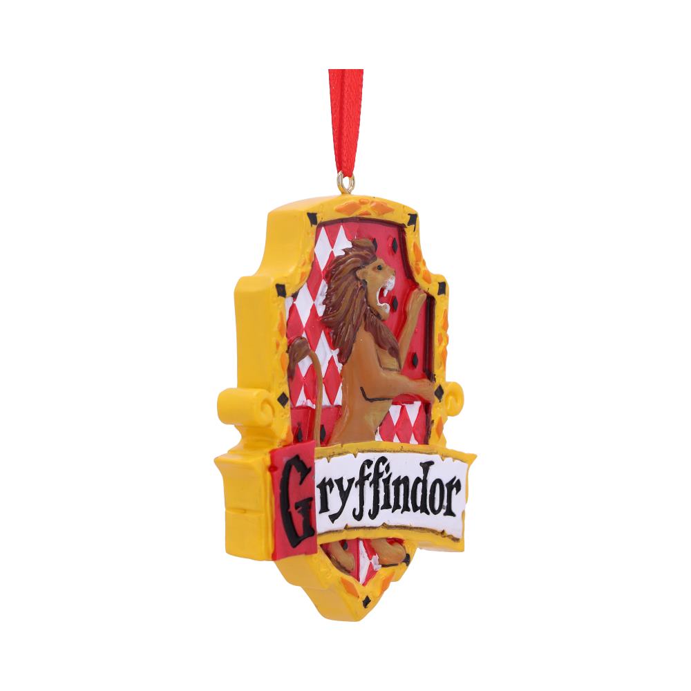 A decorative ornament depicts a yellow shield with a lion, red diamonds, and the word "Gryffindor" in bold letters. It hangs from a red ribbon, against a plain background.