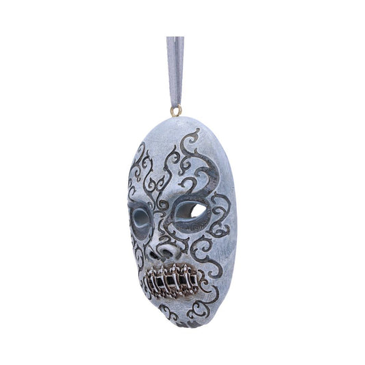 A decorative, ornate mask hangs from a string, featuring intricate scroll patterns and a stylized closed mouth design with metallic accents, set against a plain white background.