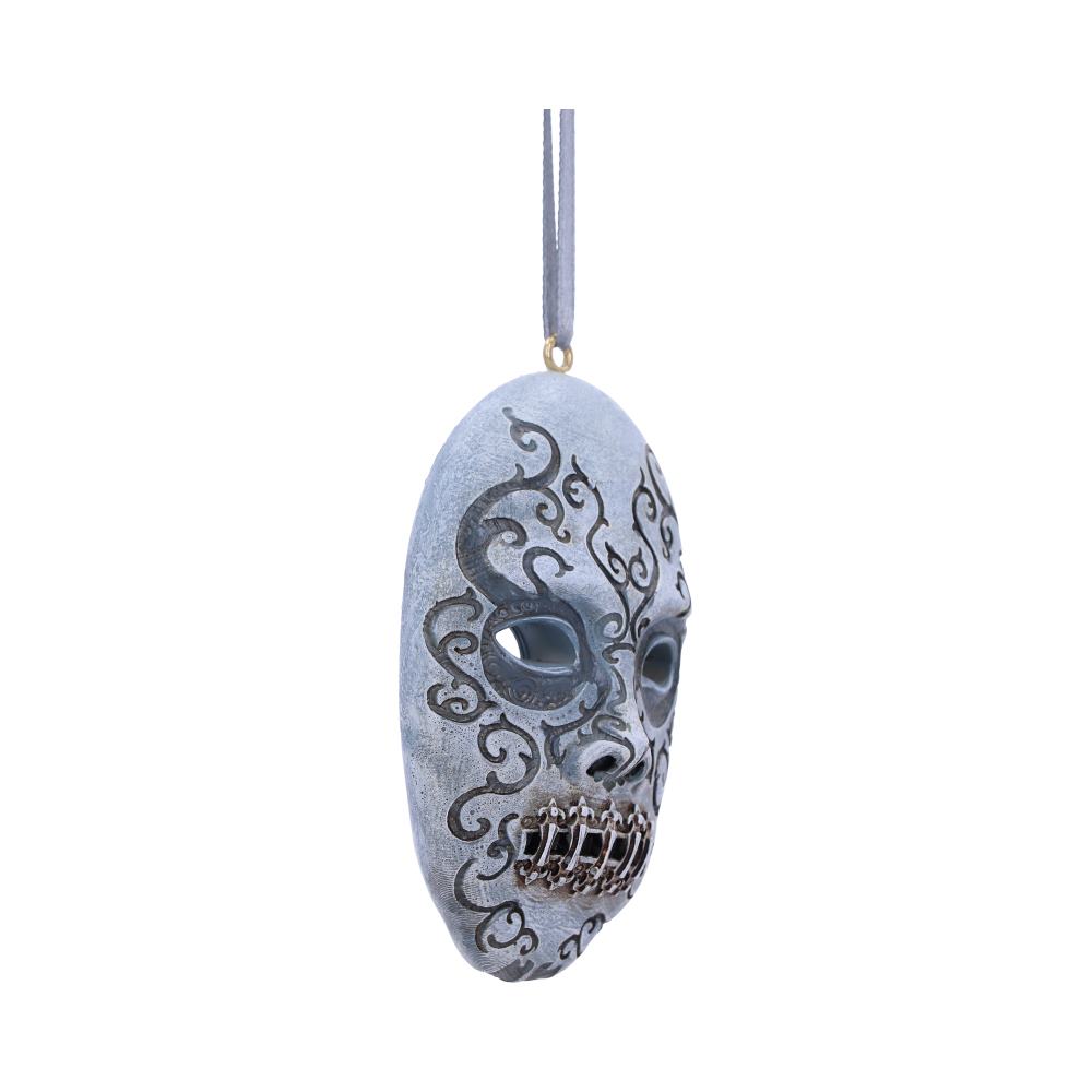 A silver decorative mask with intricate black swirls and skeletal teeth hangs by a ribbon, isolated against a white background.