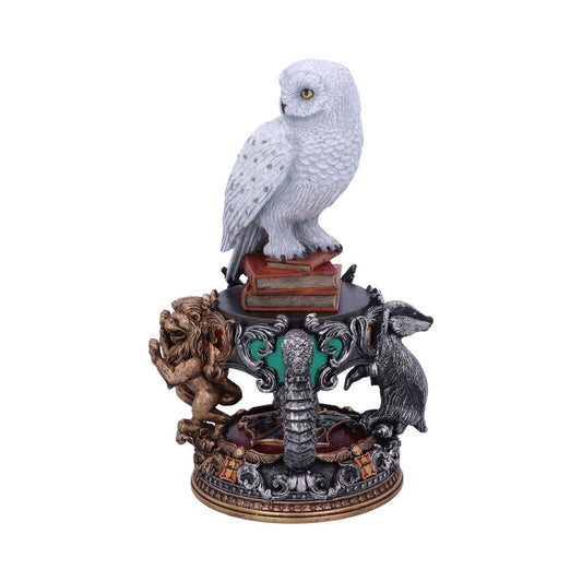 A white owl sits perched on a stack of books, surrounded by intricately designed sculptures of a lion, a badger, and an eagle, forming a decorative pedestal.