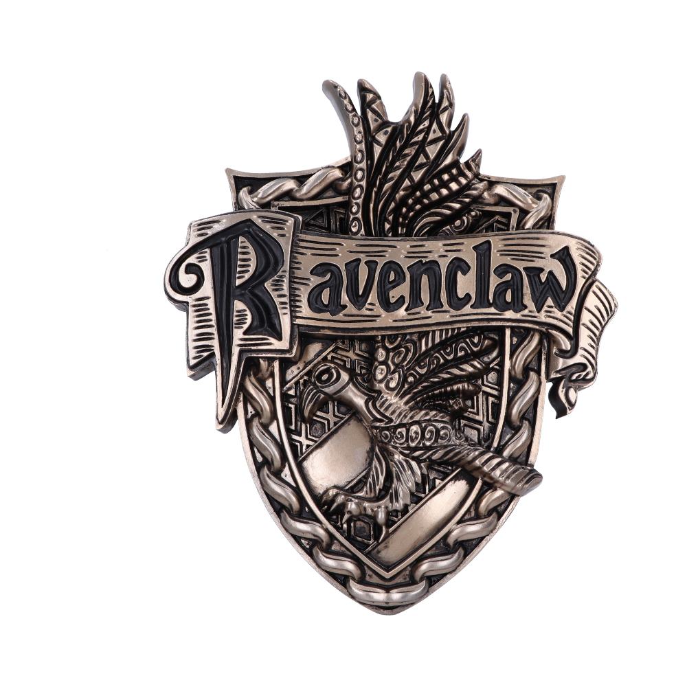 A metal badge features a stylized eagle with outstretched wings holding a scroll that reads "Ravenclaw." The intricate design includes a woven border on a shield-shaped background.