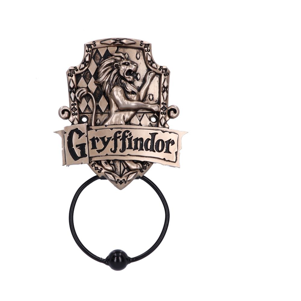 A bronze-colored door knocker features a lion emblem above the word "Gryffindor." It includes a round handle, surrounded by a decorative shield with diamond patterns, against a plain white background.