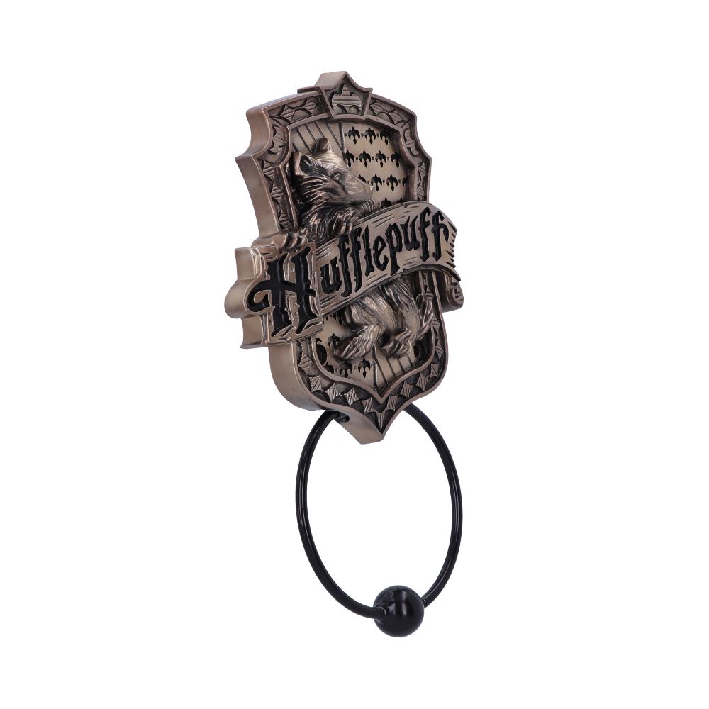 A bronze-colored door knocker with a crest, featuring a badger and the word "Hufflepuff," is mounted on a flat surface. The ring hangs below, ready for use.