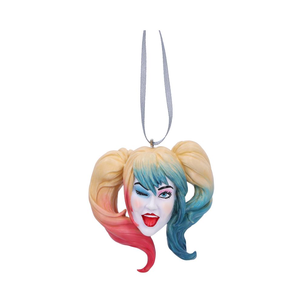 A whimsical ornament depicts a winking face with colorful pigtails in red and blue. It hangs from a ribbon, set against a plain white background.