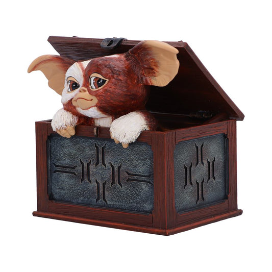 A small creature with large ears and expressive eyes peers out from an open wooden box, which has decorative inlays. The setting is plain, emphasizing the box and creature.