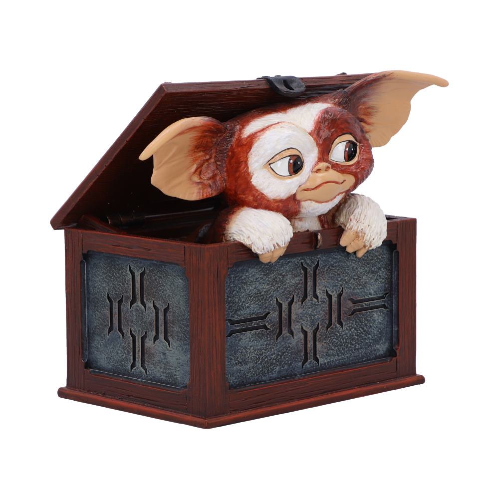 A small creature with large ears peeks out from an open wooden box with decorative panels, appearing curious. The setting is a plain background, emphasizing the playful scene.