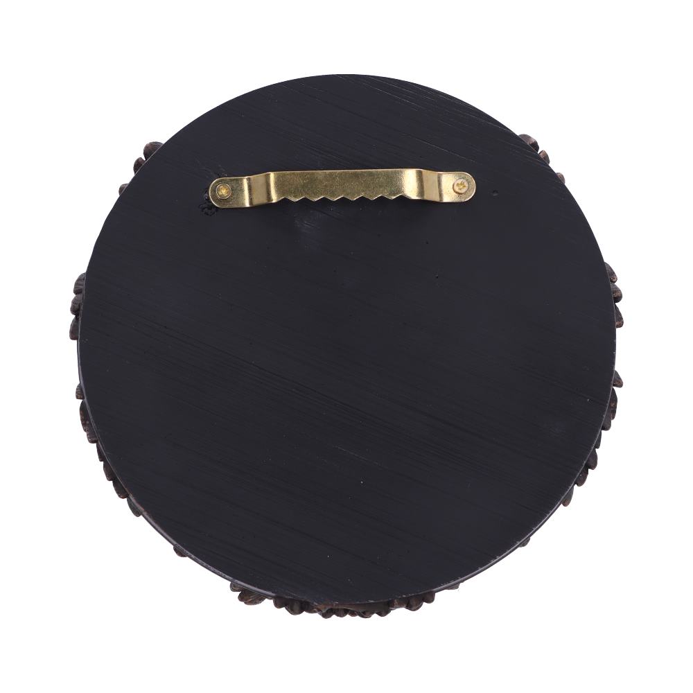 A circular wall plaque, featuring a dark surface and ornate border, hangs via a gold-toned metal hook on the back.