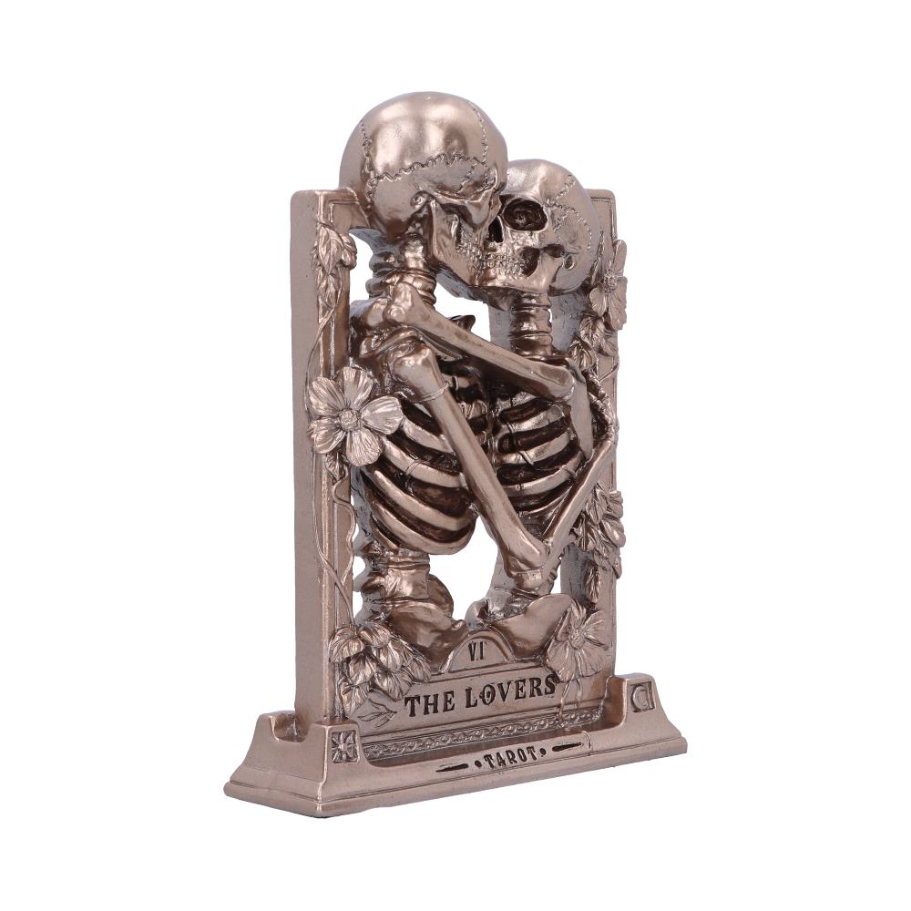 Two intertwined bronze skeletons embrace in front of a framed background with flowers. Text: “VI THE LOVERS” and “TAROT.”