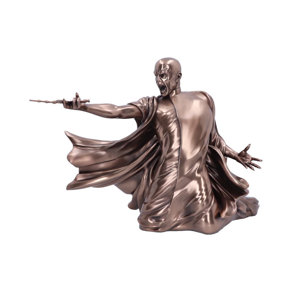 A metallic sculpture depicts a robed figure kneeling, extending a wand forward with an intense expression, in a dynamic pose, isolated against a plain background.