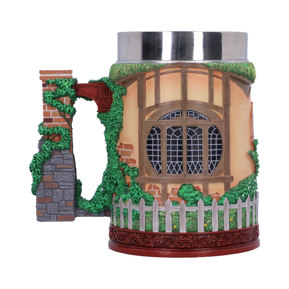A decorative ceramic mug resembling a cottage facade, featuring a detailed window, vines, brickwork, and a picket fence, with a stainless steel rim, conveying a quaint, rustic charm.