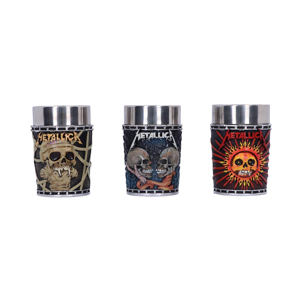Three metal shot glasses feature artistic skull designs and the word "Metallica." Each has a unique pattern: webbed skull, two skulls with bones, and a flaming sun skull, set against a plain background.