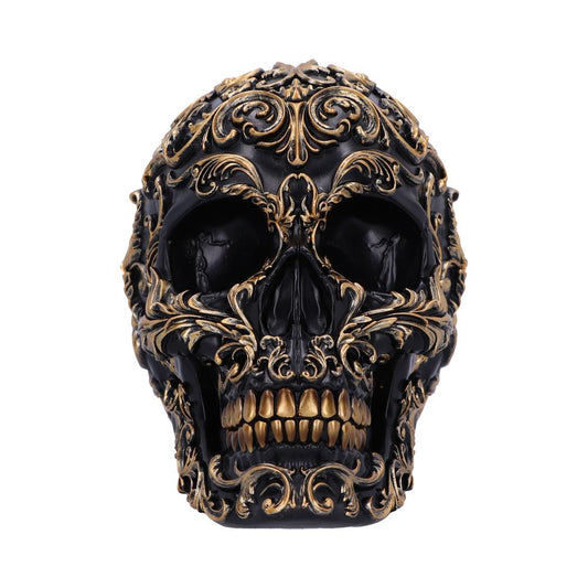 A black skull is adorned with intricate gold filigree patterns, creating an ornate and decorative appearance. The background is plain, emphasizing the skull's elaborate design.