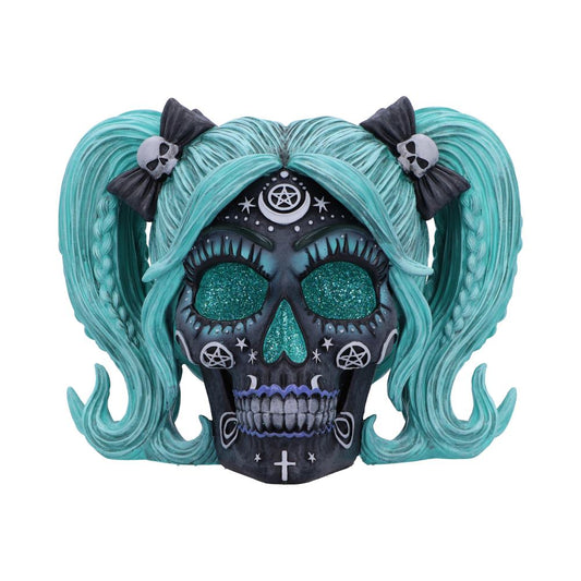 A decorative skull with turquoise braids, adorned with pentagrams and crosses, features sparkling teal eye sockets. It has black bows with skulls, creating a Gothic aesthetic.