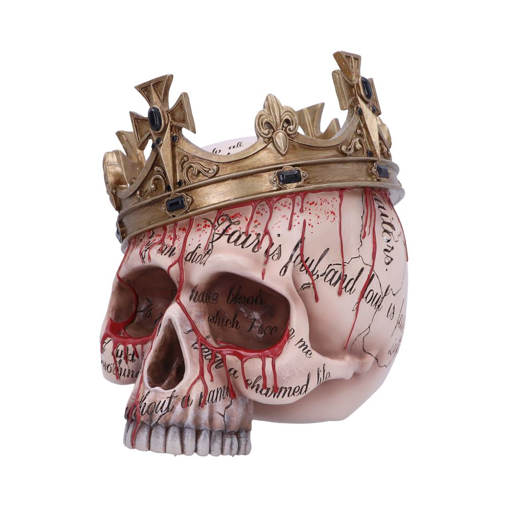 A decorated skull with a gold crown atop, features red paint resembling blood drips, and black text across the surface reading, "Fair is foul and foul is fair," in a stark white background.