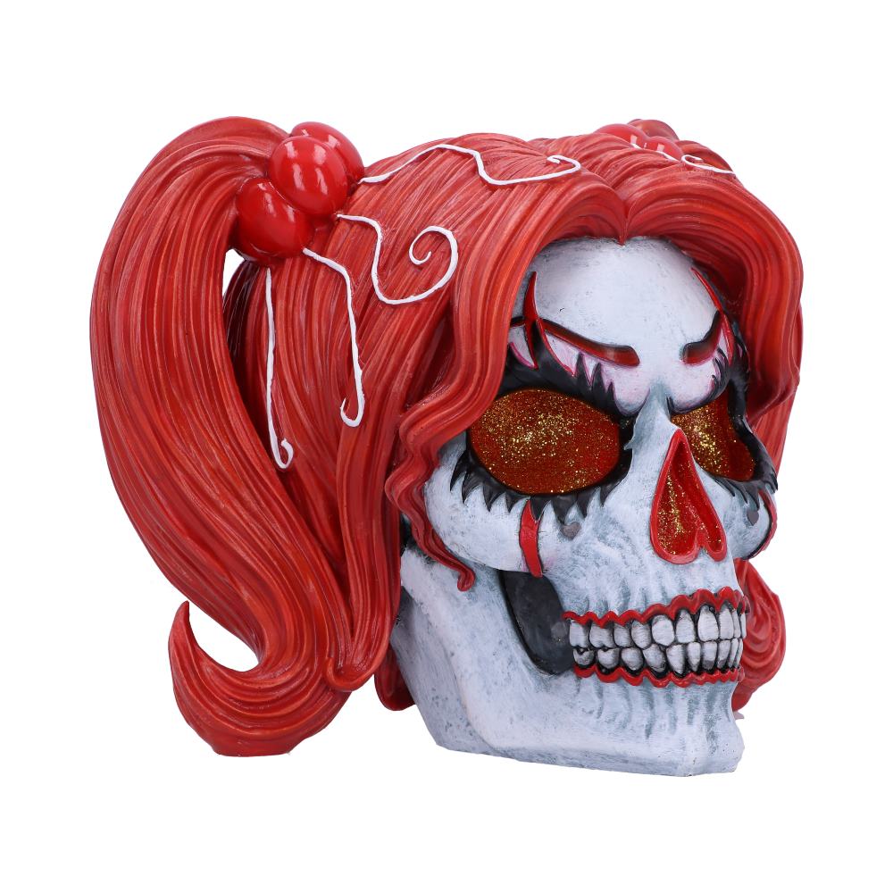 A stylized skull figurine, with red hair in pigtails, sits against a white background. The skull has painted-on features and sparkly red eyes.