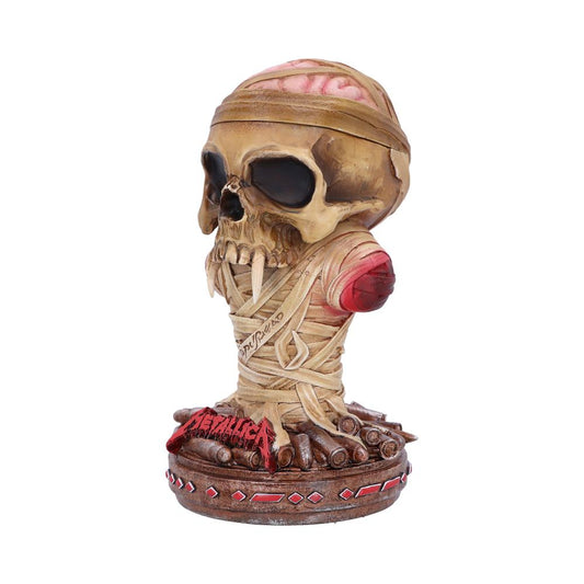 A skull with bandaged wrappings sits on a base decorated with bullets and red patterns. Visible brain tissue tops the skull. The base features the word "METALLICA" in red.