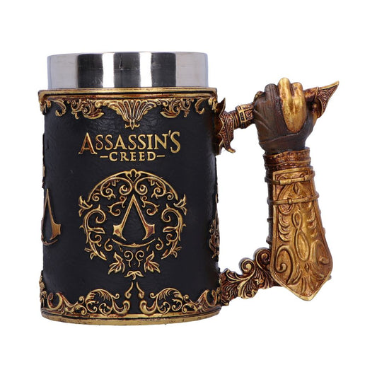 A decorative mug features a detailed medieval-style gauntlet as the handle, with gold ornate patterns on a black background. The text reads "ASSASSIN'S CREED" above an emblematic symbol.