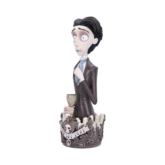A stylized figurine of a pale, wide-eyed man holds a goblet, wearing a suit. He stands in a decorative base with swirling patterns and a skull motif. Text: "VAN DORT."