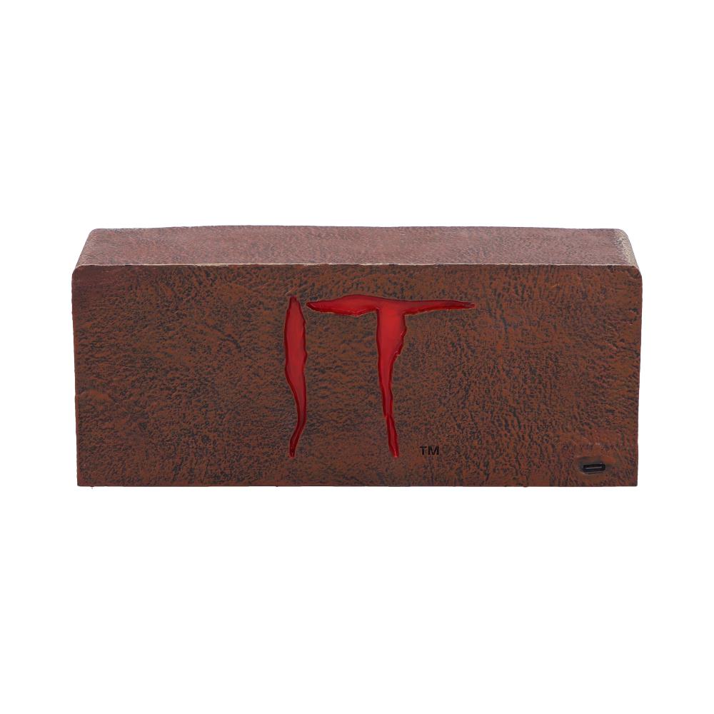 A rectangular brown block features red lettering "IT" on its front. The texture resembles rusted metal, and a trademark symbol is visible. The setting is plain and unobtrusive.
