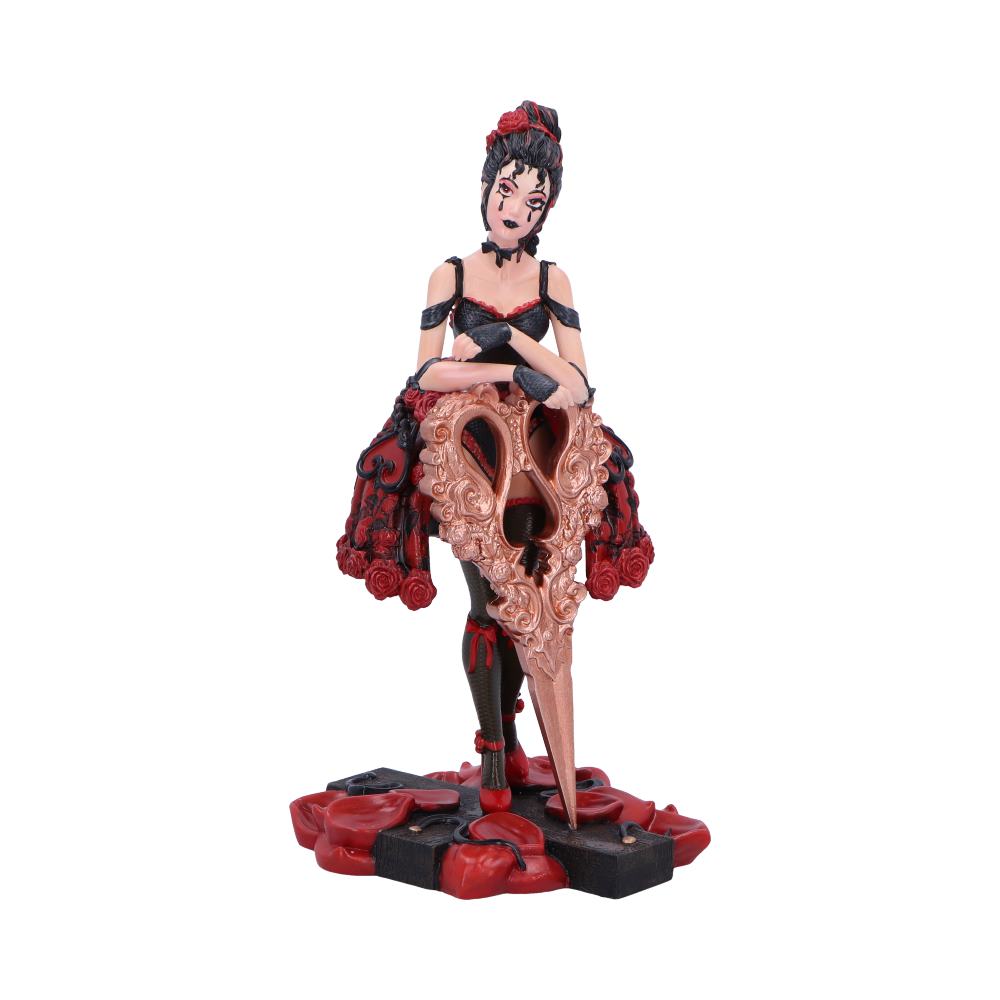 A dark-haired figurine, wearing a red and black dress, leans on a large, ornate scissor sculpture; the base is a dark cross with red accents.