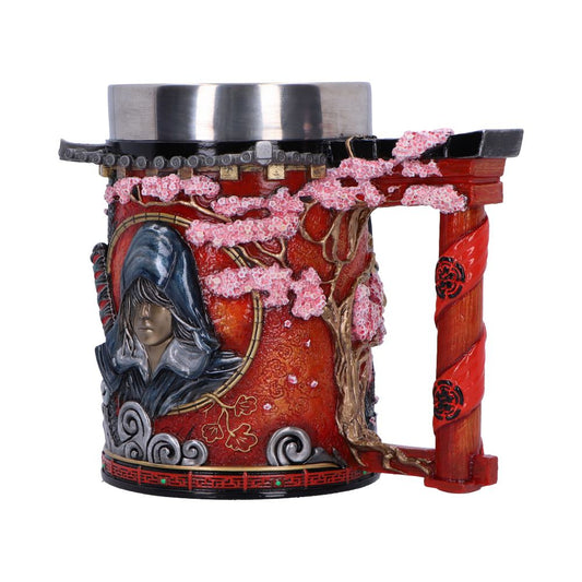 A decorative mug features a hooded figure embossed on the side, surrounded by cherry blossom branches. The handle resembles a red, twisted column. The mug has a metal rim on top.