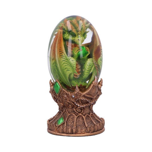 Green dragon curled inside a glass-like egg atop an ornate bronze pedestal adorned with green gemstones, set against a plain white background.