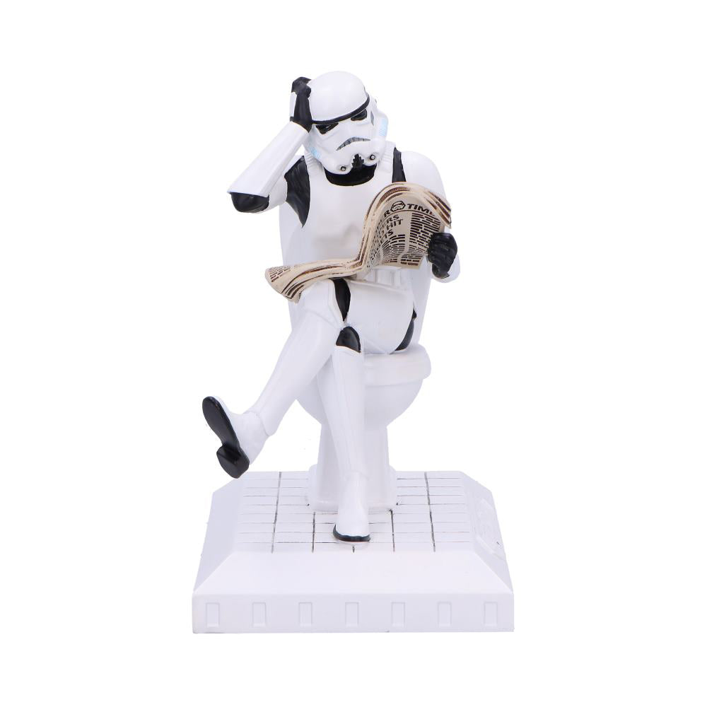 Stormtrooper figurine sits on a toilet reading a newspaper, one hand to its helmet, legs crossed on a small tile platform against a white background.