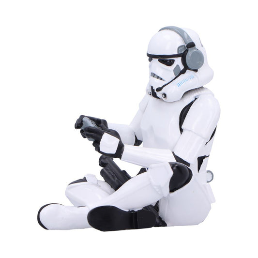 Stormtrooper action figure sits cross-legged holding a game controller and wearing gray headphones against a plain white background.