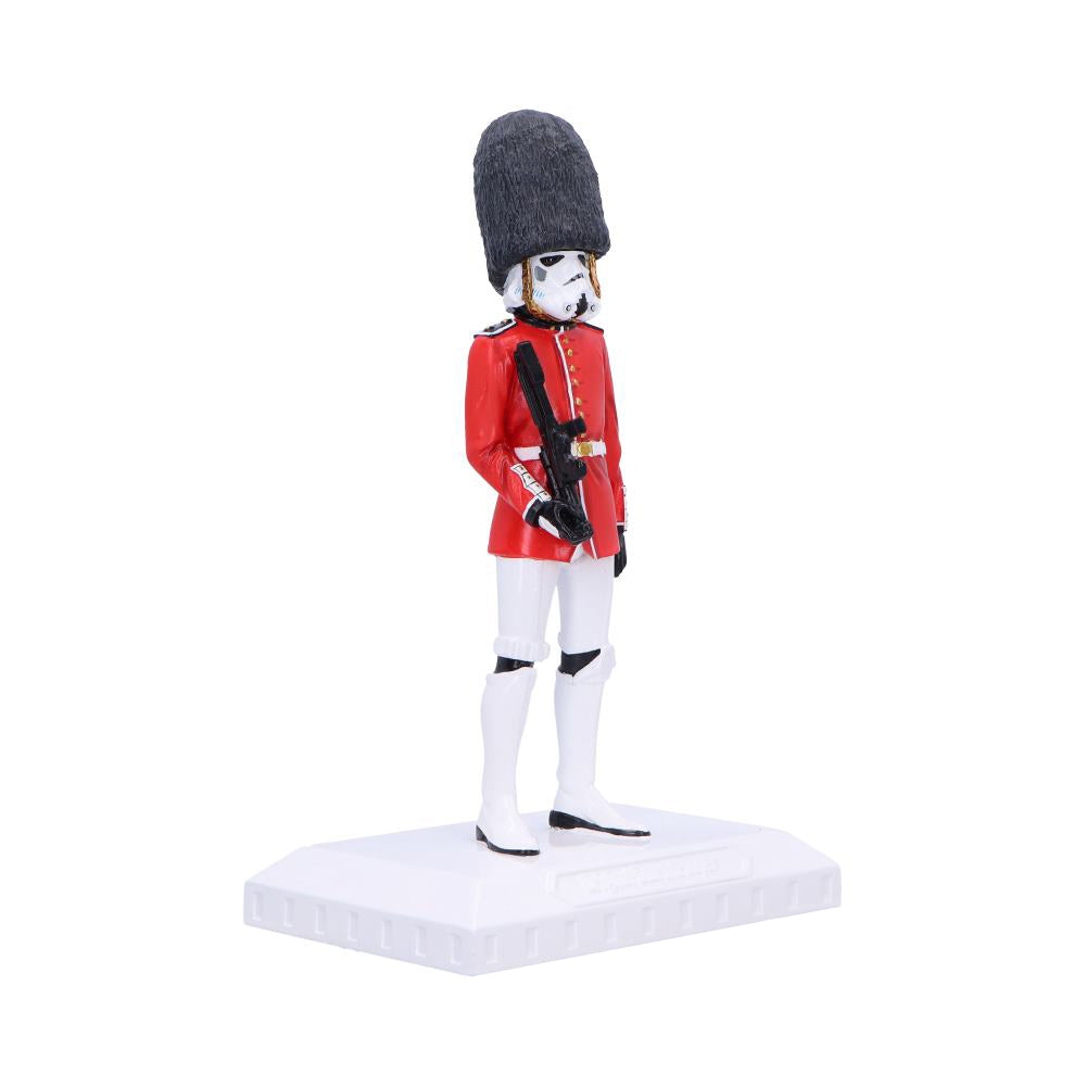 Figure of a British guard in a red tunic and tall bearskin hat with a Stormtrooper mask stands holding a blaster on a white base against a white background.