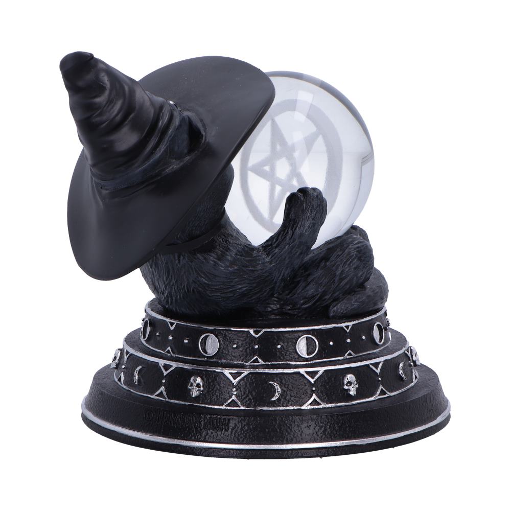 Black cat figurine wearing a pointed witch hat holds a crystal ball etched with a pentagram while sitting on a base patterned with moon phases and skulls against white.