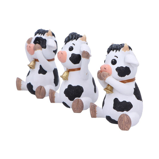 Three small black and white cow figurines sit in a row, each covering eyes, ears, and mouth respectively, wearing gold bells on brown collars against a plain white background.