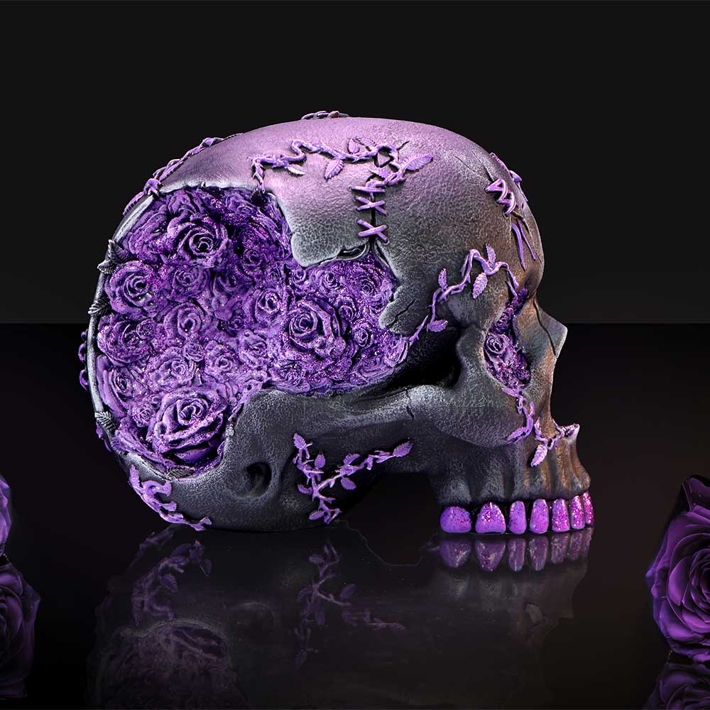 Decorative skull filled with purple roses sits on a reflective black surface, stitched vine details and cracks cross its bone, glittery purple teeth, dark gradient background.
