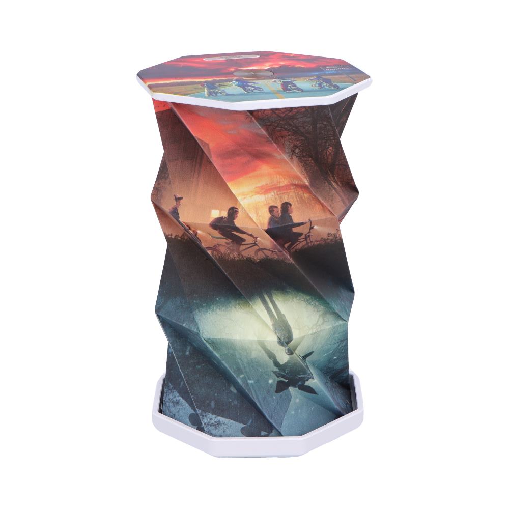 Collapsible octagonal stool stands upright, displaying an accordion-pleated printed sleeve showing cyclists at sunset and an underwater mirrored figure on a white studio background.