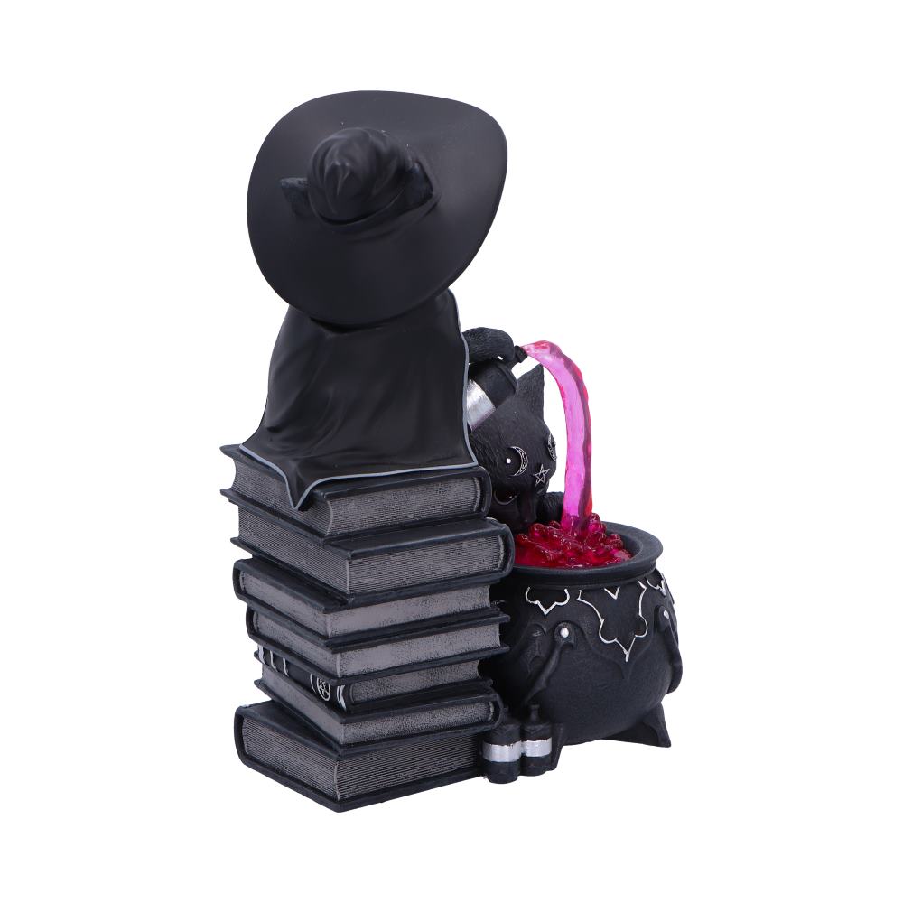 Witch figurine wearing a wide black hat leans over stacked books, pouring a bright pink potion into a bubbling cauldron filled with red liquid on a white background.
