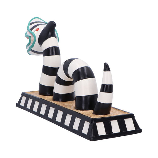 Striped black-and-white ceramic serpent sculpture rising in three curved segments from a rectangular black-and-white bordered cork base, head tilted back with teal ruffle and a red eye against white background.