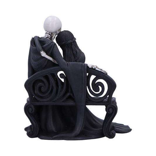 Skeletal figure and dark-haired woman sit entwined on an ornate black bench, skeleton draped in a cloak with an arm around her, draped robes pooling on a white background.