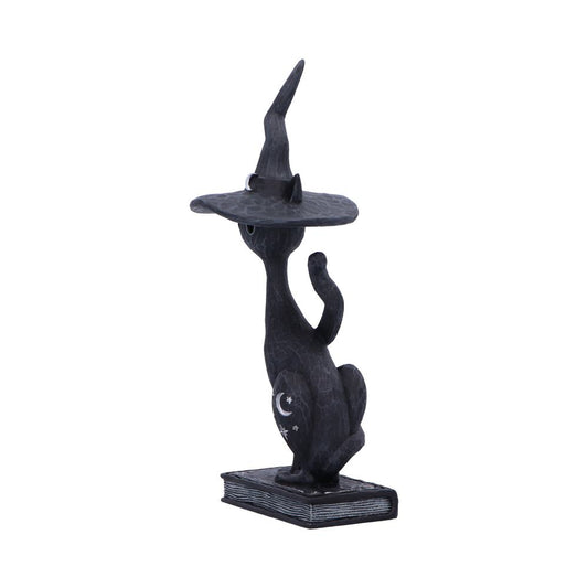 Black cat figurine wearing a tall pointed witch hat sits on a closed book, one paw raised, crescent moon and stars painted on its flank against a plain white background.