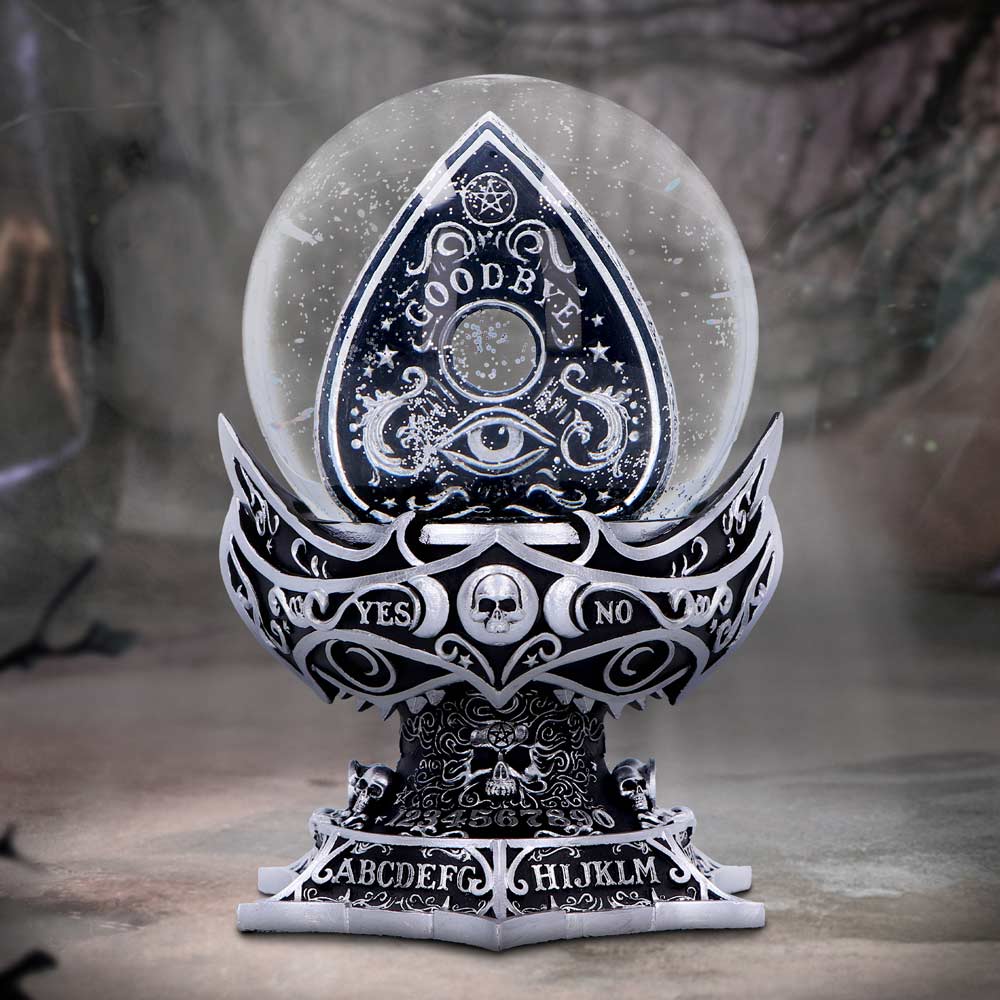 Crystal ball sits on an ornate Ouija-style base showing a planchette reading GOODBYE inside the globe and base embossed with YES NO and the letters ABCDEFG HIJKLM in a dim, foggy room.