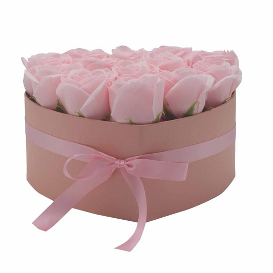 Heart-shaped pink box holds a dense arrangement of pale pink roses, wrapped with a matching satin ribbon bow, displayed on a plain white background.